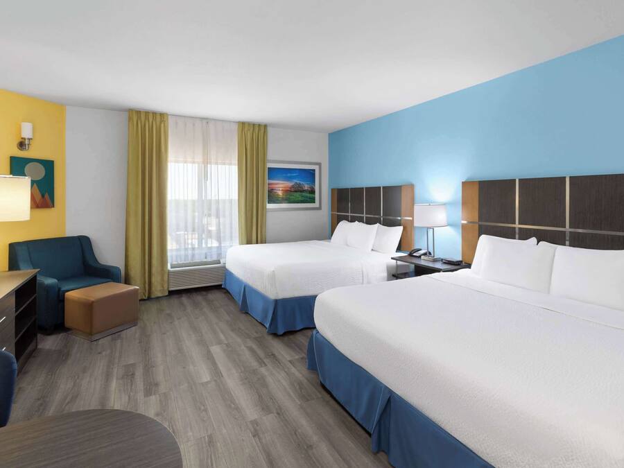 A hotel room with two beds, a desk, a chair, a lamp, and a window with curtains.