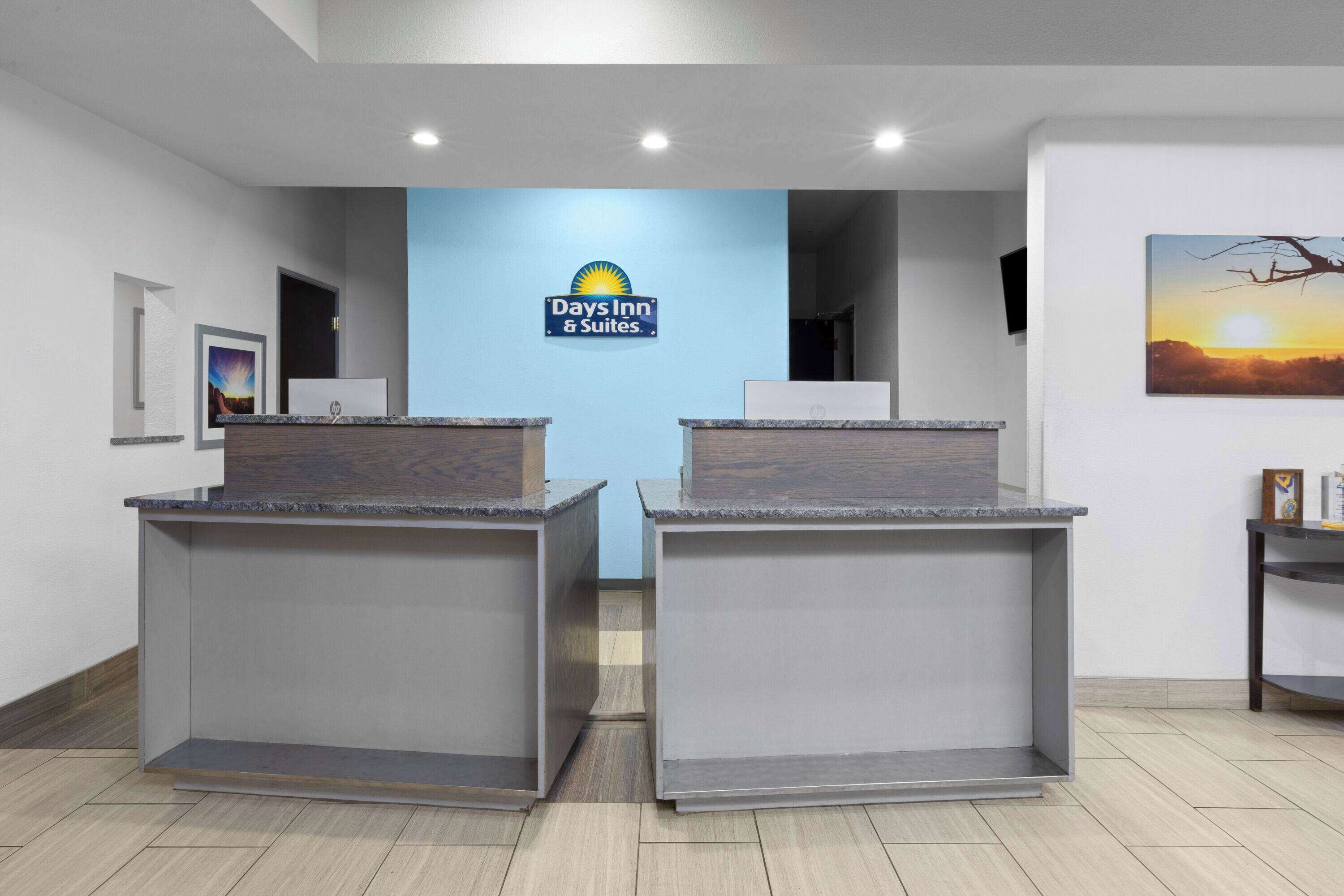 A reception area with a blue wall and a Days Inn & Suites sign. There are two reception desks with a modern design.