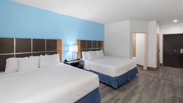 A hotel room with two beds, a nightstand, a lamp, and a door.