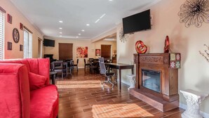 Un salón amplio con un sofá rojo, una chimenea, un televisor montado en la pared y un comedor al fondo.