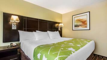 Una habitación de hotel con una cama grande, dos lámparas de noche, una mesita de noche con un teléfono y un cuadro enmarcado en la pared.