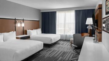 A hotel room with two beds, a desk, a chair, and a window with curtains.