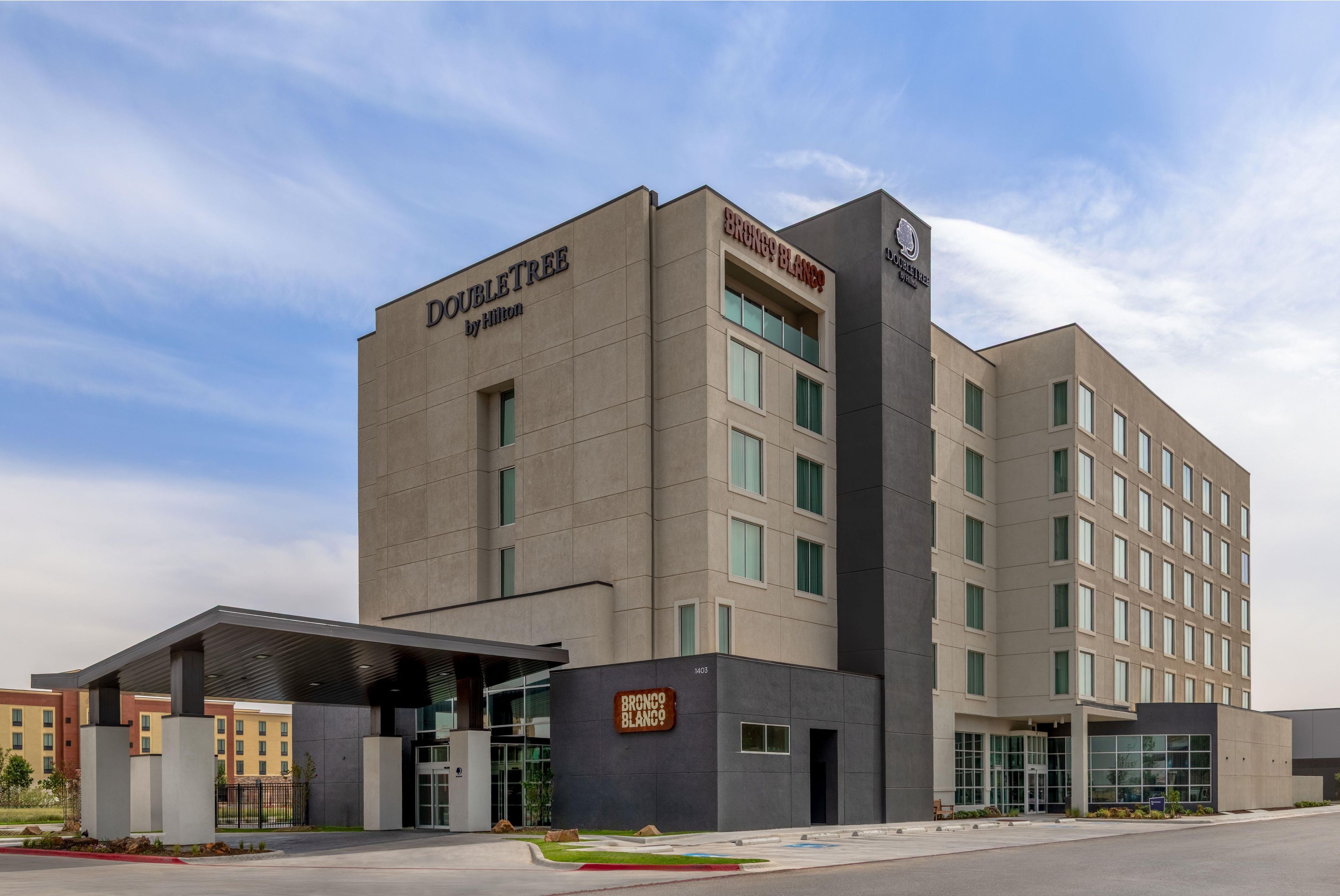 A modern hotel building with a prominent 'Doubleday' sign, multiple windows, and a gated entrance.