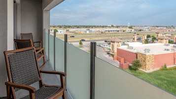 A balcony with two wicker chairs, a view of a parking lot, and buildings in the distance.