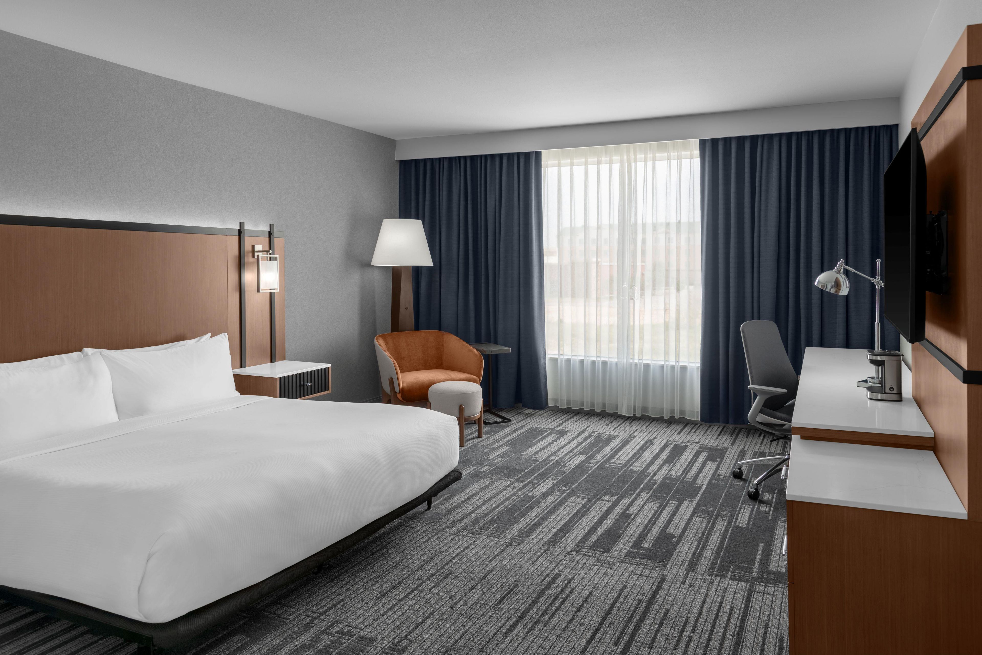 A hotel room with a large bed, a desk, a chair, a lamp, and a TV.