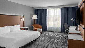 A hotel room with a large bed, a desk, a chair, a lamp, and a TV.