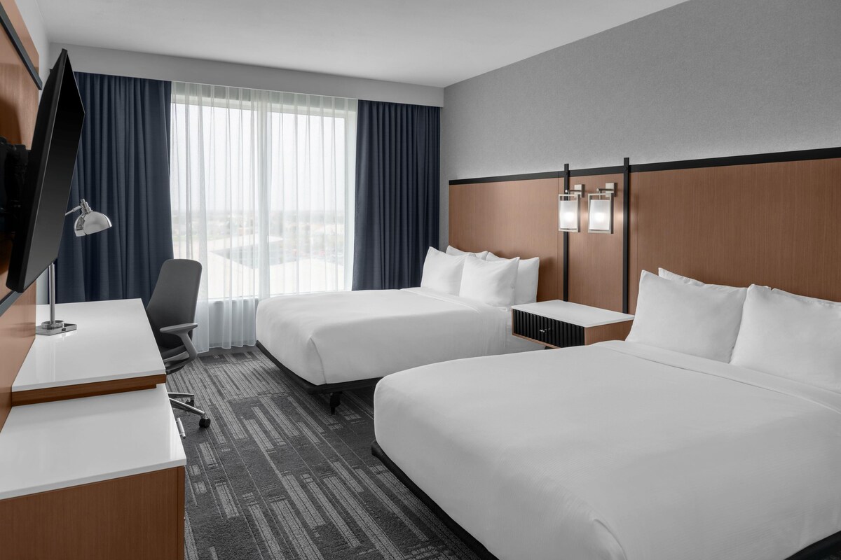 A hotel room with two beds, a desk, a chair, a TV, and a window with curtains.