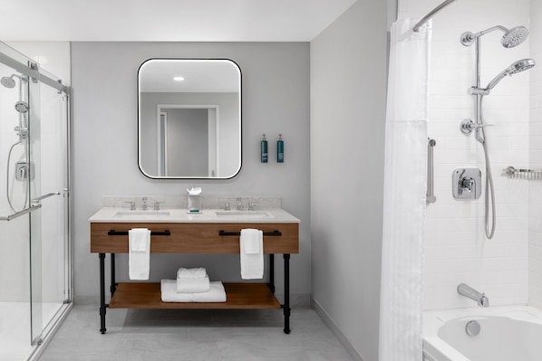 A modern bathroom with a double sink vanity, a large mirror, a shower with multiple heads, and a bathtub. - DoubleTree by Hilton Midland West Loop I-250 (Midland)
