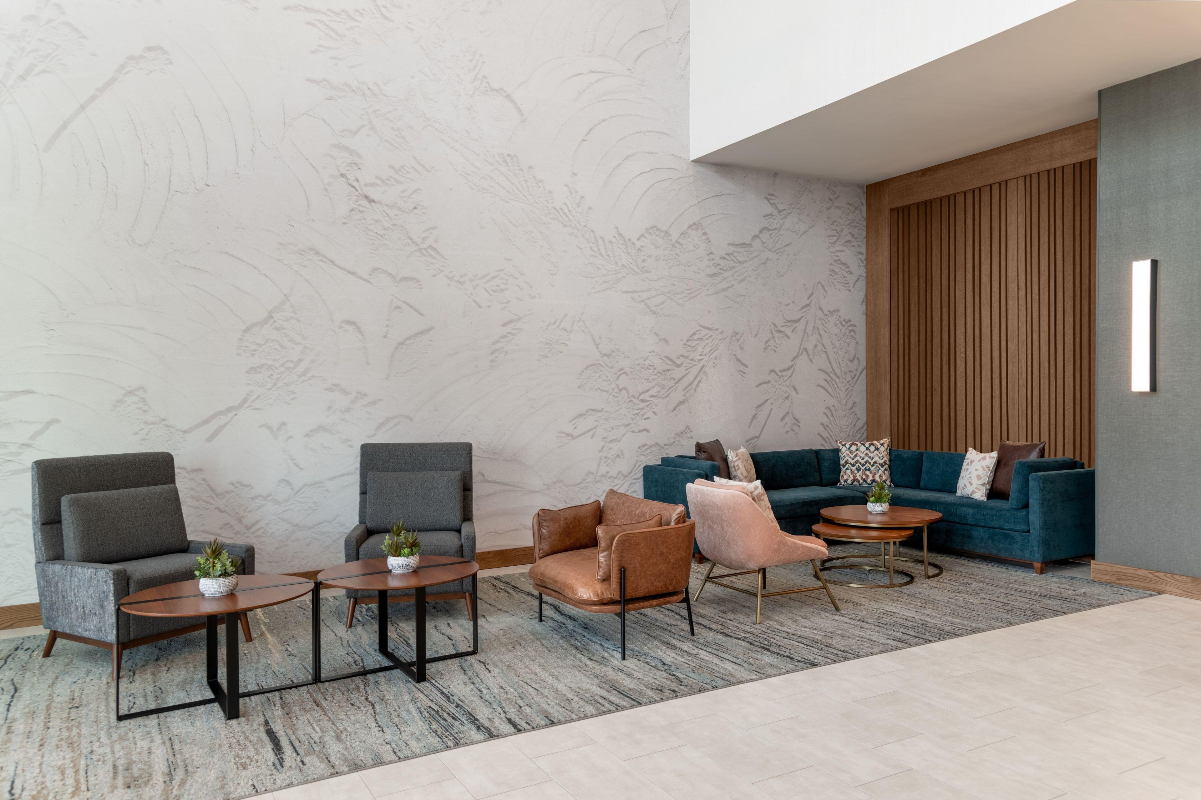 A modern lounge area with seating arrangements, including sofas and chairs, a patterned wall, and a wooden panel accent.