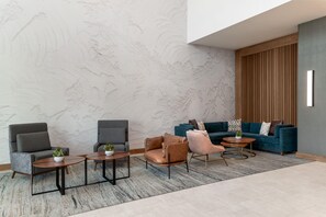 A modern lounge area with seating arrangements, including sofas and chairs, a patterned wall, and a wooden panel accent. - DoubleTree by Hilton Midland West Loop I-250 (Midland)