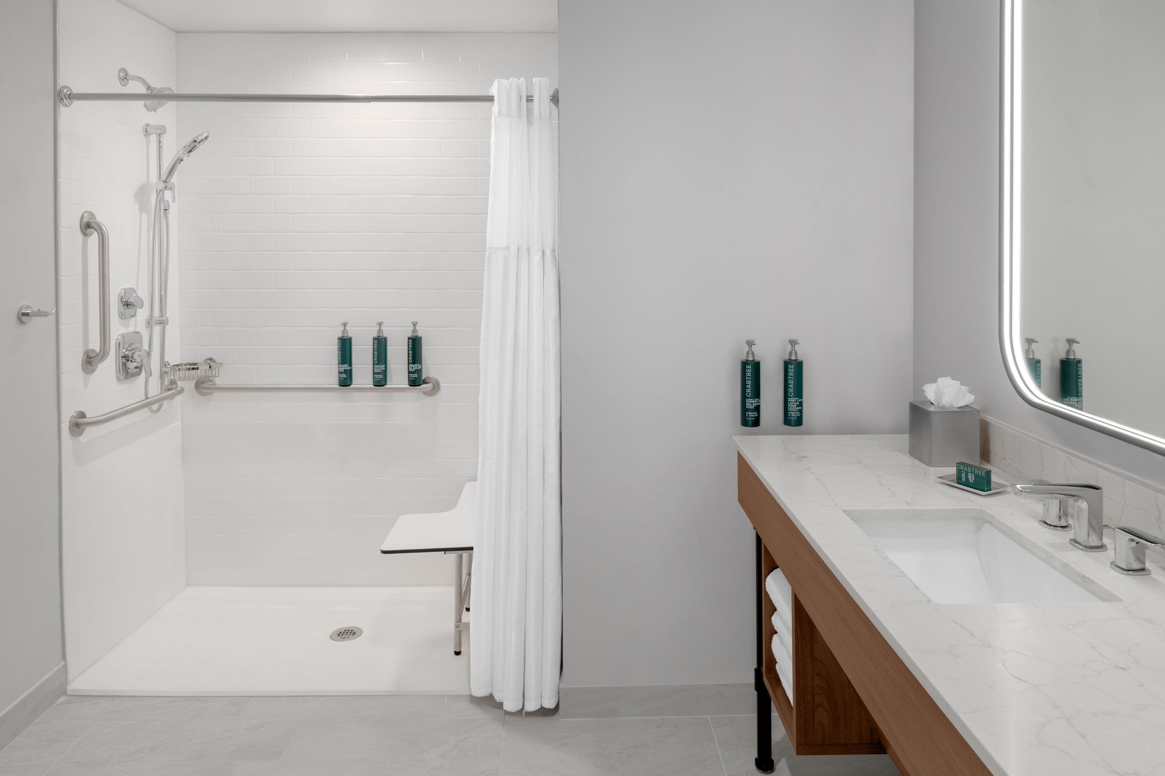 Ein modernes Badezimmer mit barrierefreier Dusche, Haltegriffen, einem Waschtisch mit Spiegel und Pflegeprodukten.