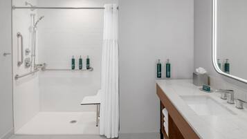 Ein modernes Badezimmer mit barrierefreier Dusche, Haltegriffen, einem Waschtisch mit Spiegel und Pflegeprodukten.