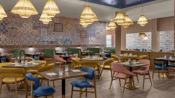 A restaurant interior with multiple dining tables, chairs, and hanging pendant lights.
