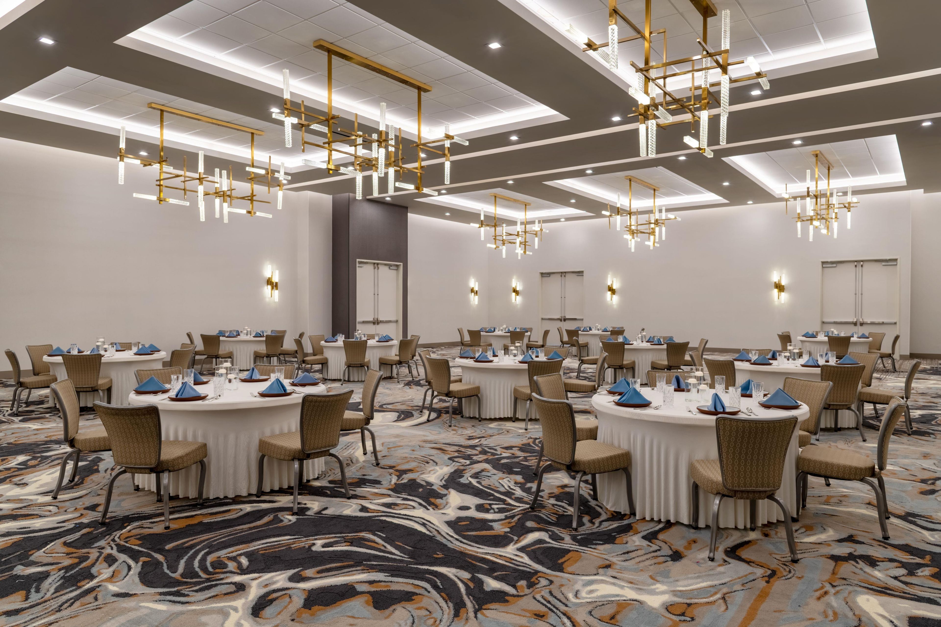 A conference room with round tables, chairs, and modern chandeliers.
