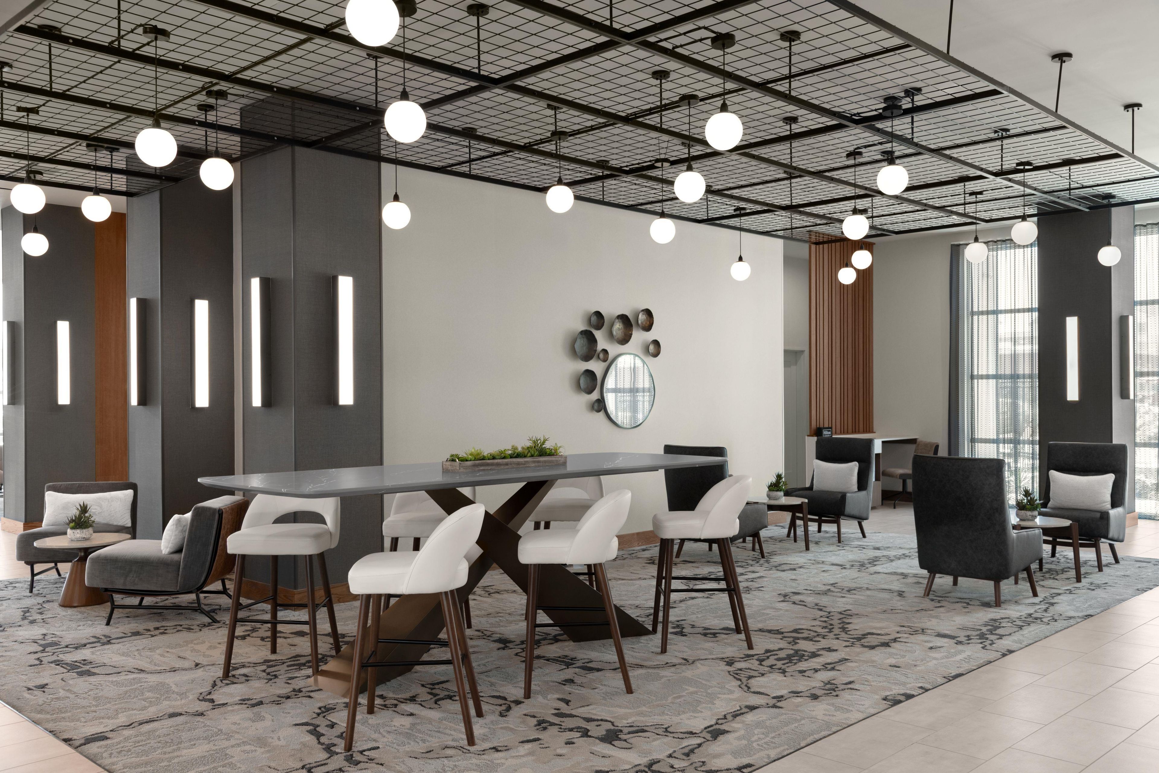 A modern conference room with a long table, white chairs, and a patterned rug.
