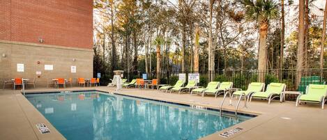 A swimming pool with lounge chairs and a brick building in the background.
