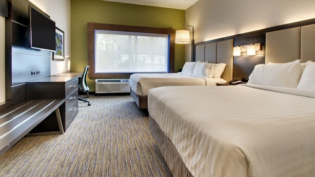 Een hotelkamer met twee bedden, een bureau, een flatscreen televisie en een raam met uitzicht op bomen.