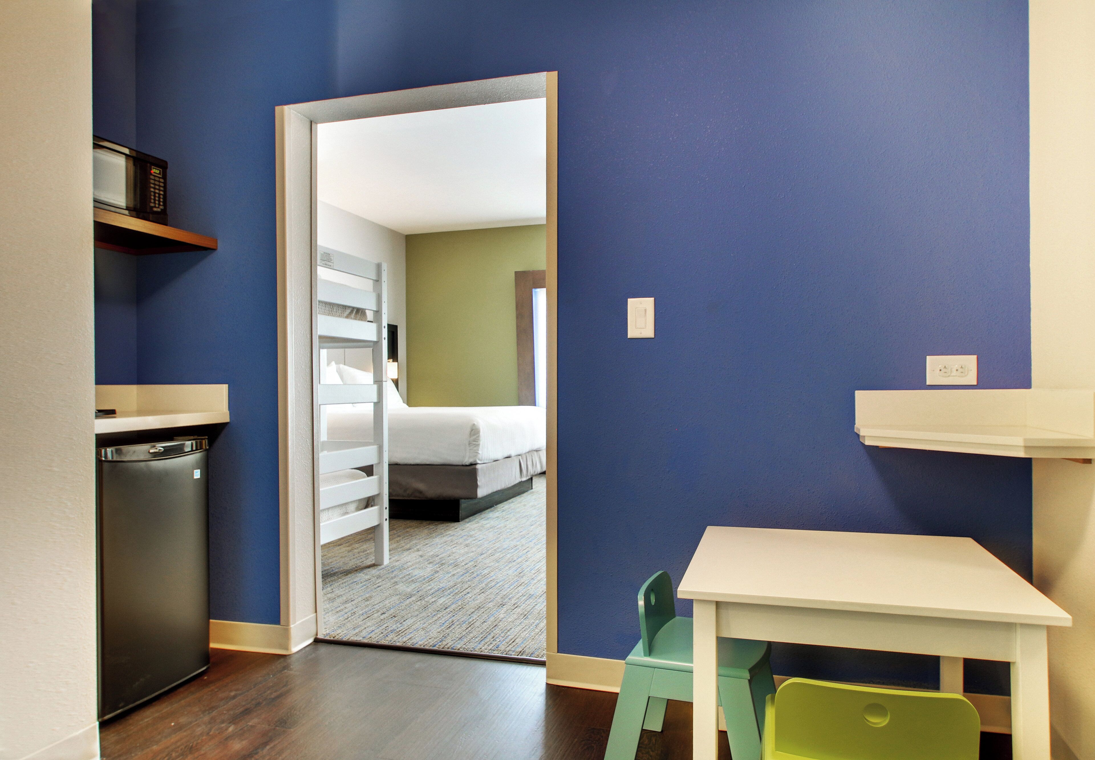 A compact hotel room with a kitchenette, a bed, and a small table.