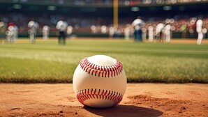 Een honkbal op een zandige infield, met een onscherpe tribune op de achtergrond.