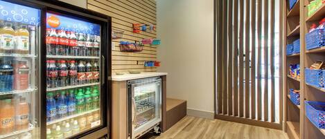 A beverage refrigerator stocked with various drinks, a small display case with snacks, and a wooden slat partition.
