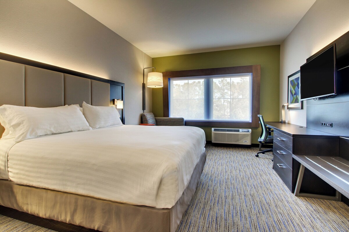 A hotel room with a bed, desk, chair, TV, and window.