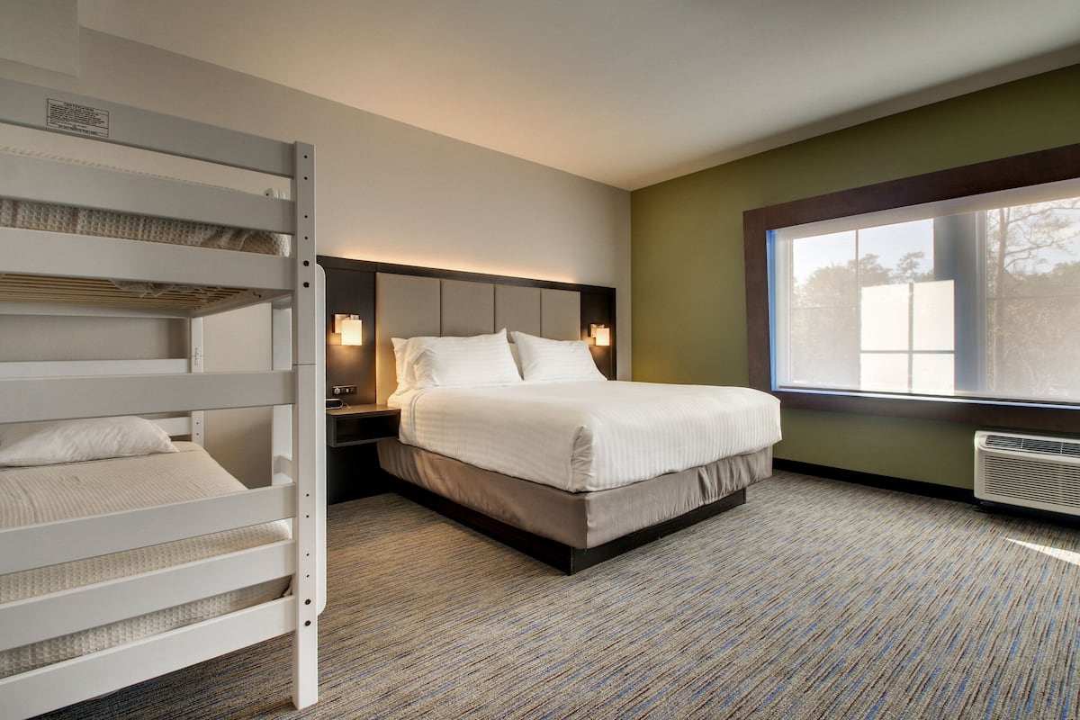 Hotelkamer met een stapelbed, een enkel bed, een nachtkastje met lamp en een groot raam met uitzicht.