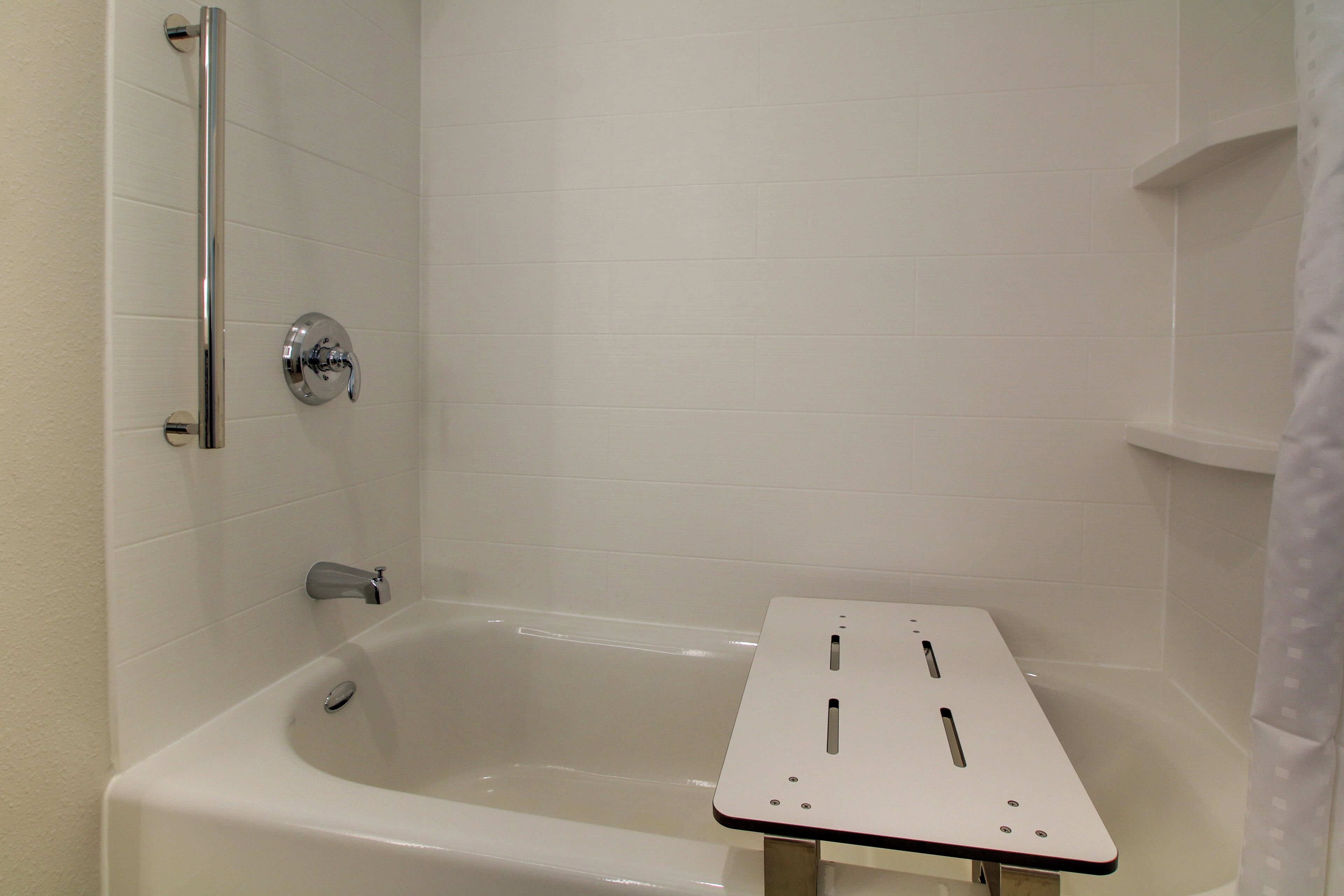 Een badkamer met een badkuip, douche en een betegelde wand.