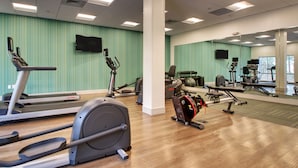 Une salle de sport équipée d’appareils de cardio, de miroirs et d’un téléviseur fixé au mur.