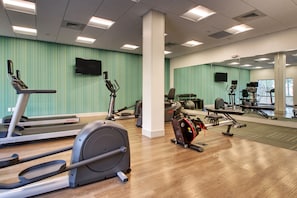 Een sportschool met cardioapparatuur, spiegels en een televisie aan de muur.