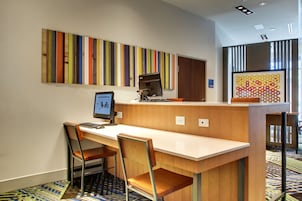 A modern office space with a long desk, two chairs, a computer, and a colorful abstract painting on the wall.