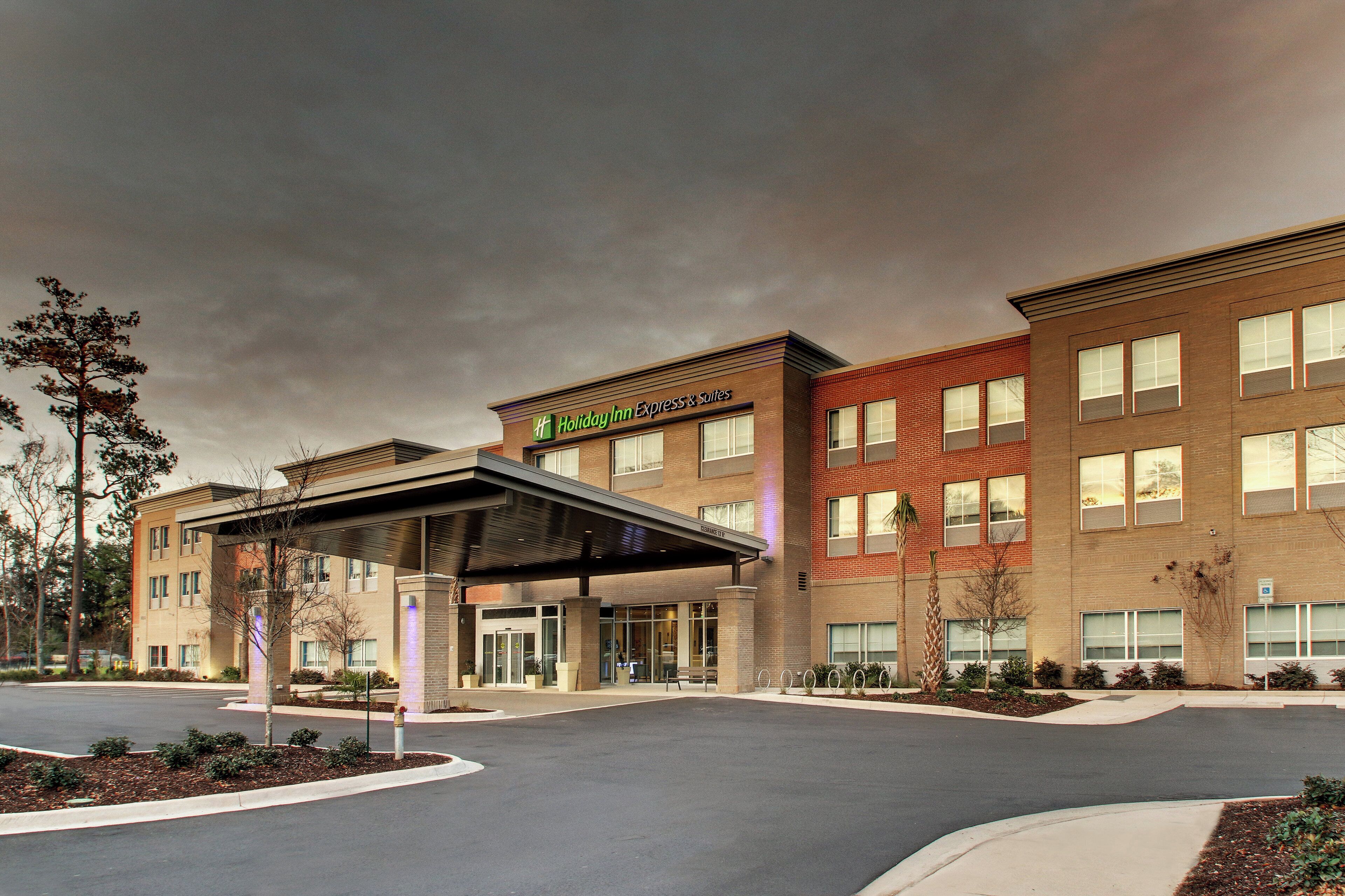 A Holiday Inn Express Suites hotel with a covered entrance, multiple windows, and a landscaped driveway.