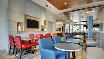 A modern dining area with red and blue seating, a flat-screen TV, and a kitchen in the background.
