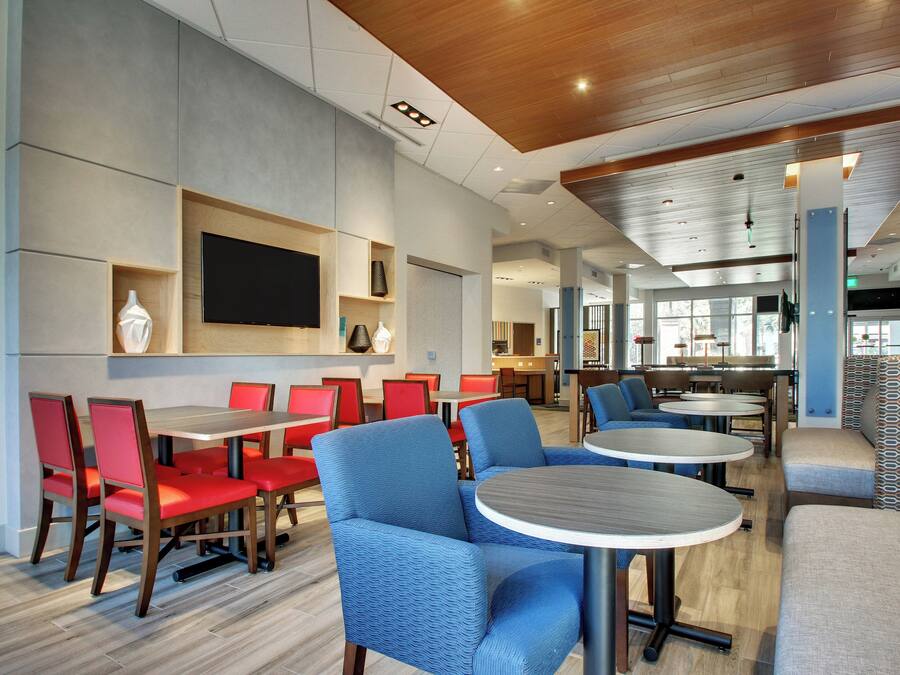 A modern dining area with red and blue seating, a flat-screen TV, and a kitchen in the background.