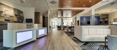 Un hall de hotel con mostradores de recepción, zonas de estar y techo de madera.