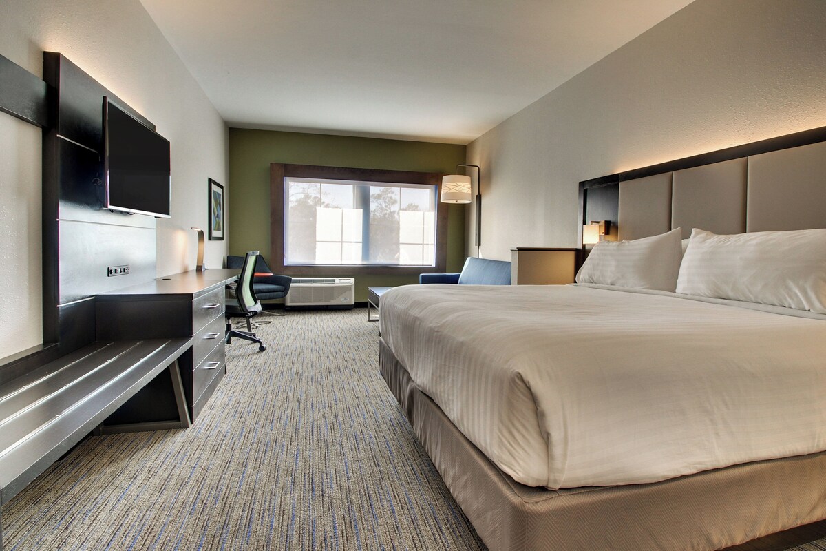A hotel room with a bed, desk, chair, TV, and a window.