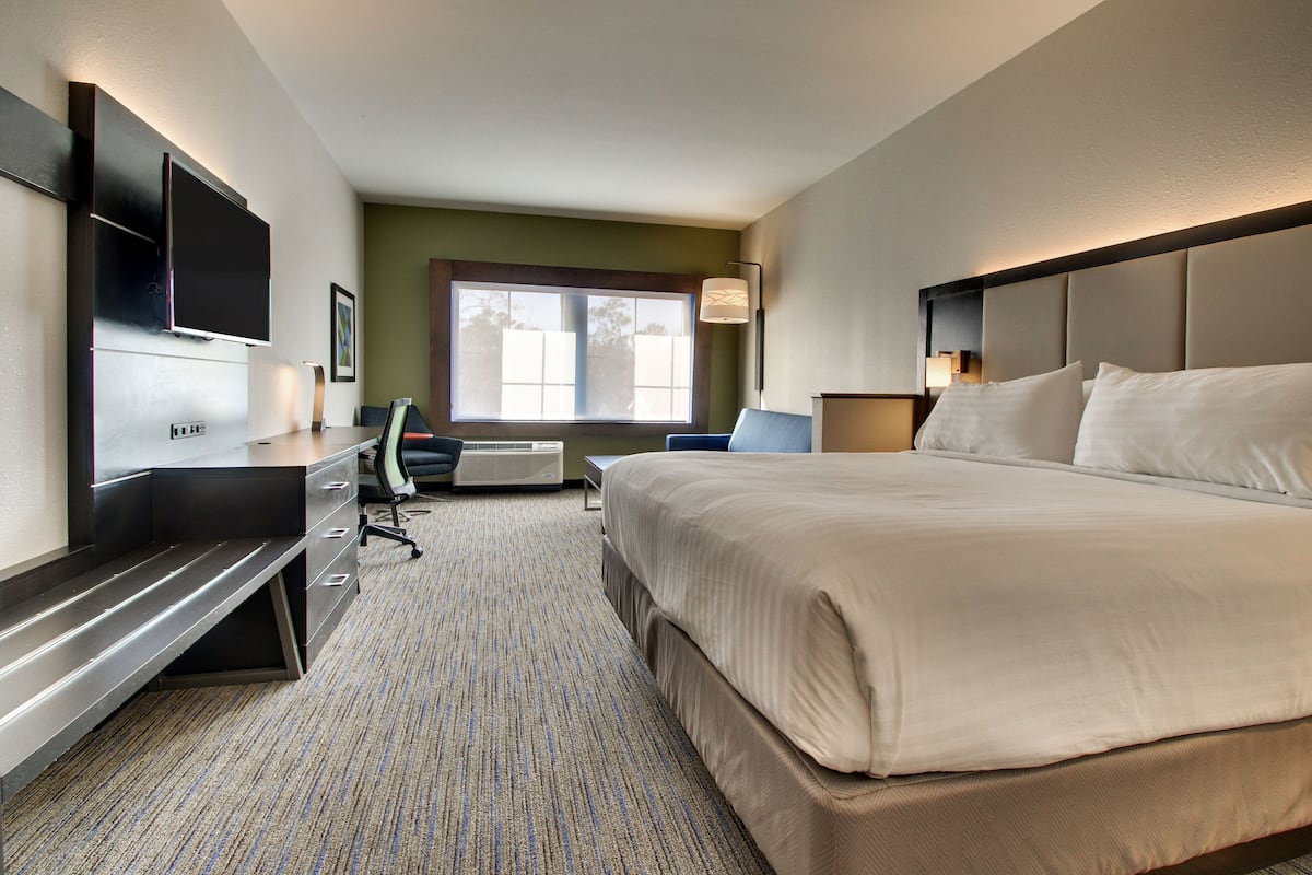 Hotelkamer met een groot bed, bureau met stoel, flatscreen televisie aan de wand en een raam met uitzicht op bomen.