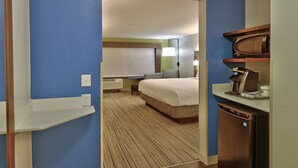 A hotel room with a bed, a desk with a coffee maker, and a view of another room. - Holiday Inn Express and Suites Broomfield by IHG (Broomfield)