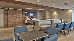 Un hall d’hôtel moderne avec un comptoir d’accueil, un espace salon et une horloge au mur.