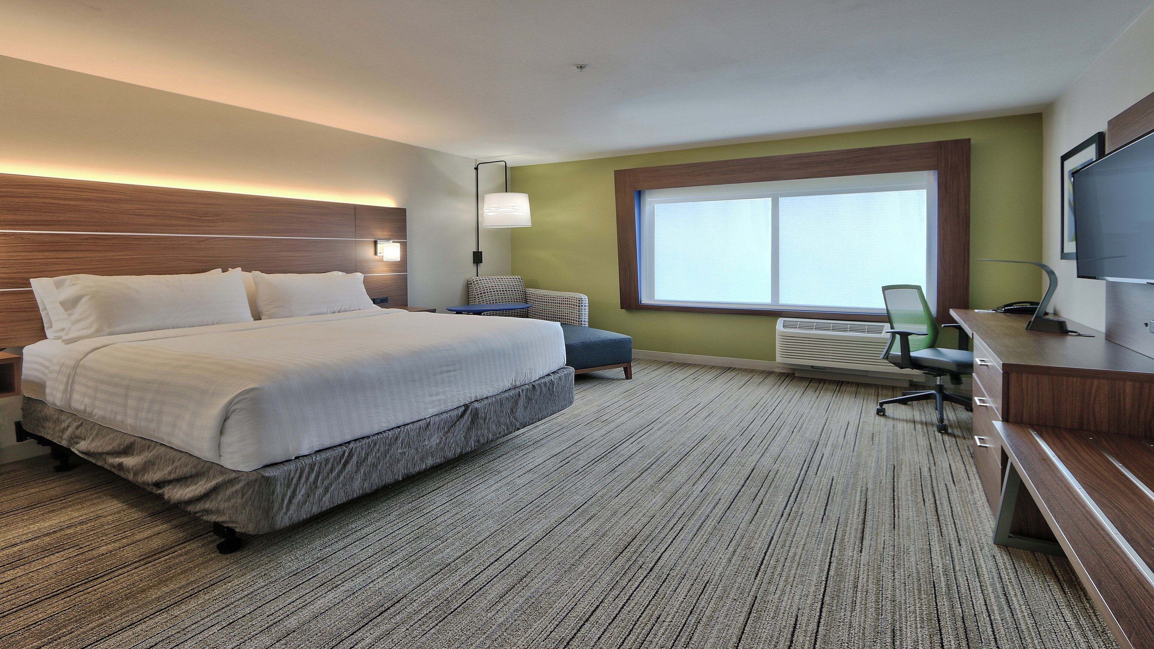 Habitación de hotel con cama, escritorio, silla, televisor y ventana.