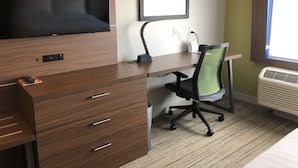 A hotel room with a wooden desk, a chair, a flat-screen TV, a framed abstract artwork, and a window with blinds. - Holiday Inn Express and Suites Broomfield by IHG (Broomfield)