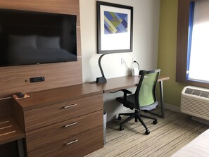 A hotel room with a wooden desk, a chair, a flat-screen TV, a framed abstract artwork, and a window with blinds. - Holiday Inn Express and Suites Broomfield by IHG (Broomfield)
