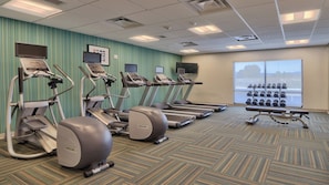 Une salle de sport équipée de tapis de course, de vélos elliptiques et d’une série de haltères.
