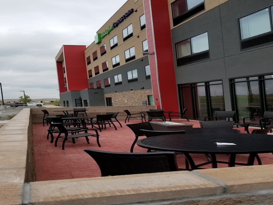 Un área de estar al aire libre con mesas y sillas, un edificio de fachada roja y gris, y un gran ventanal con el número 11401.