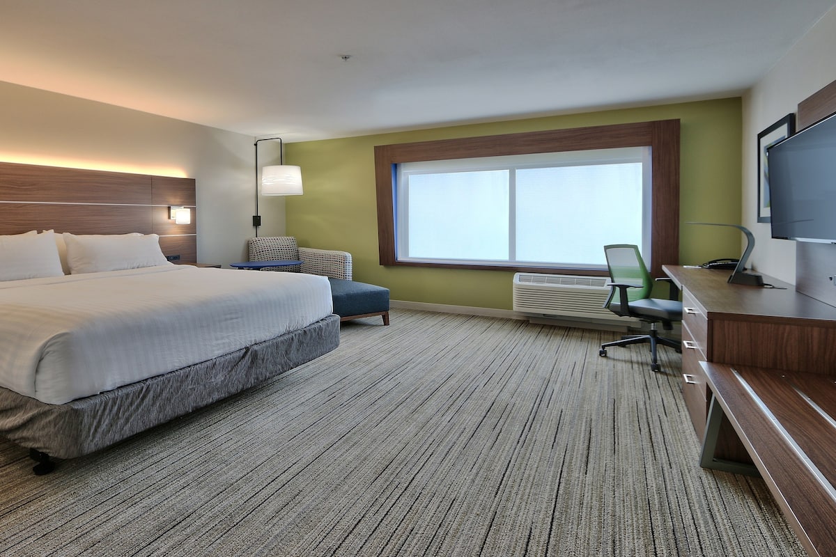 A hotel room with a large bed, a desk, a chair, a television, and a window.