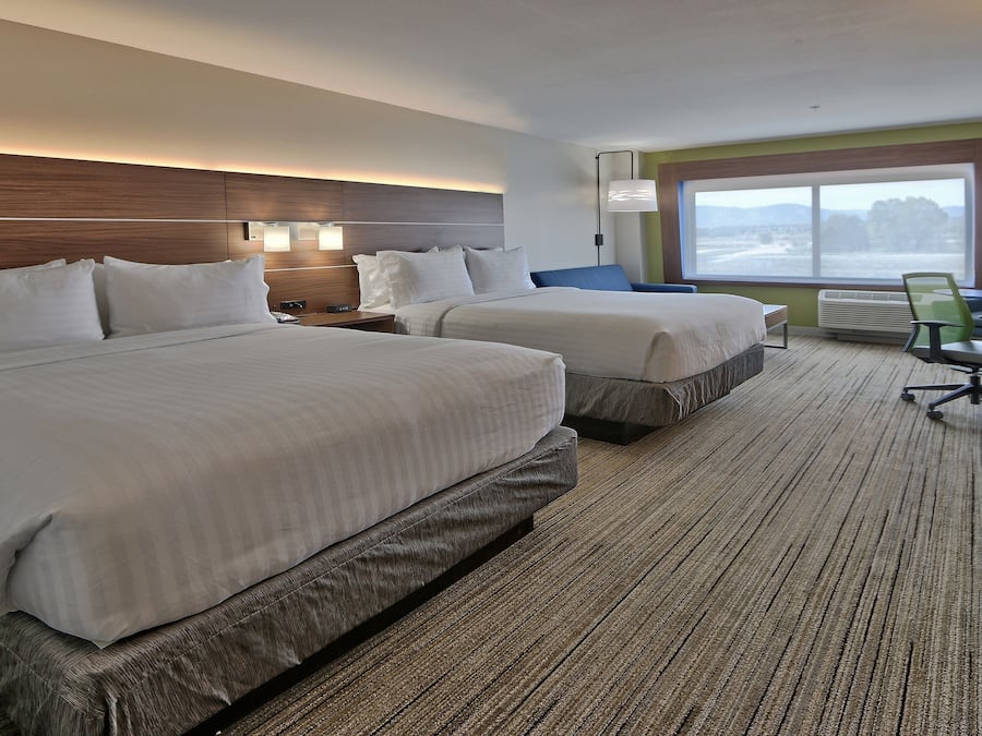 Habitación de hotel con dos camas, un escritorio, una silla y un ventanal grande.