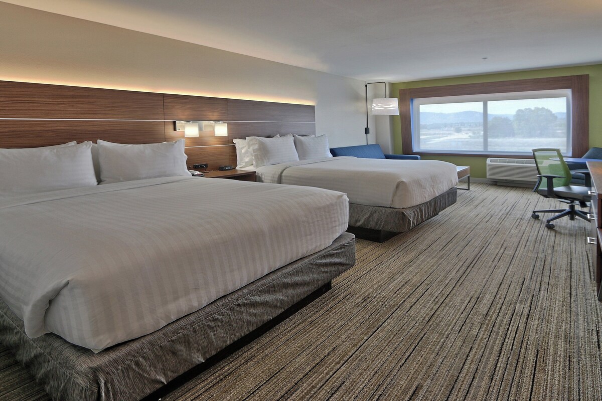 A hotel room with two beds, a desk, a chair, and a large window.