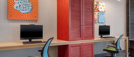A workspace with two desks, two chairs, and a red cabinet. There are two monitors on the desks, and a colorful artwork is on the wall.