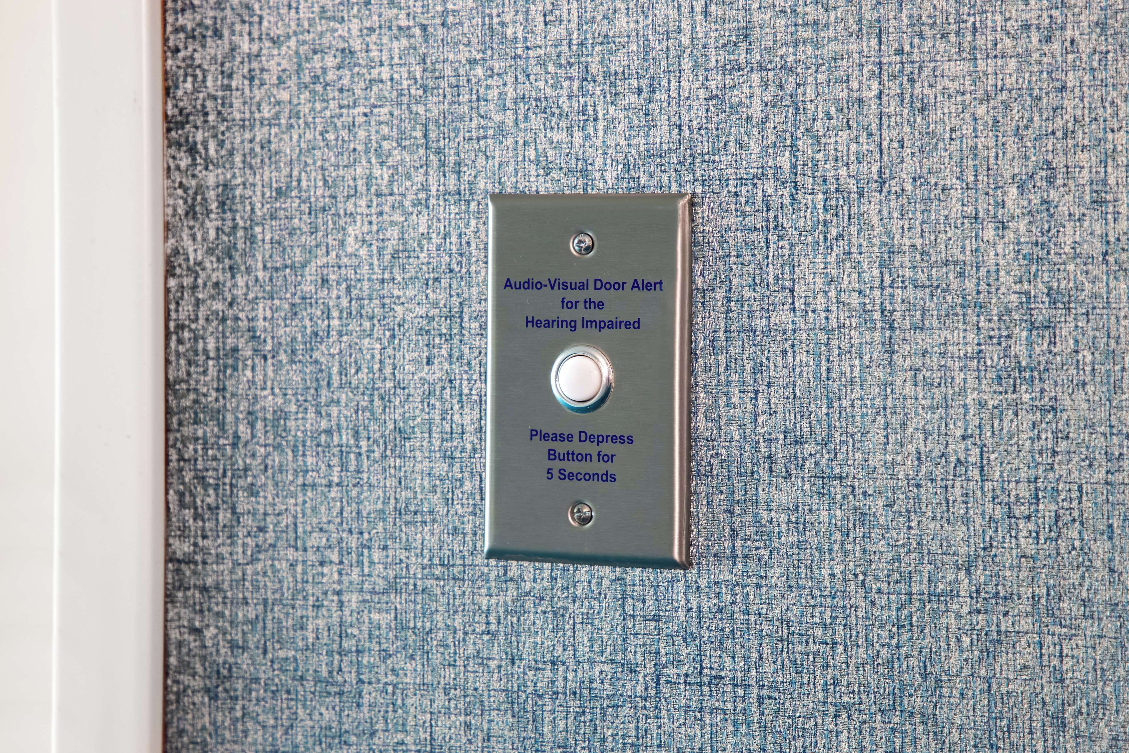 A metal plate with a button and text indicating an audio-visual door alert for the hearing impaired.