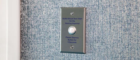 A metal plate with a button and text indicating an audio-visual door alert for the hearing impaired.
