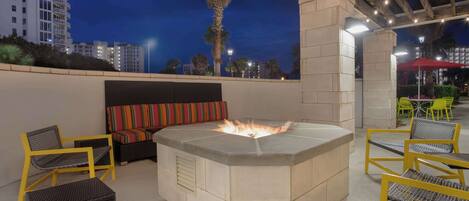 An outdoor seating area with a fire pit, yellow chairs, and a cushioned bench.